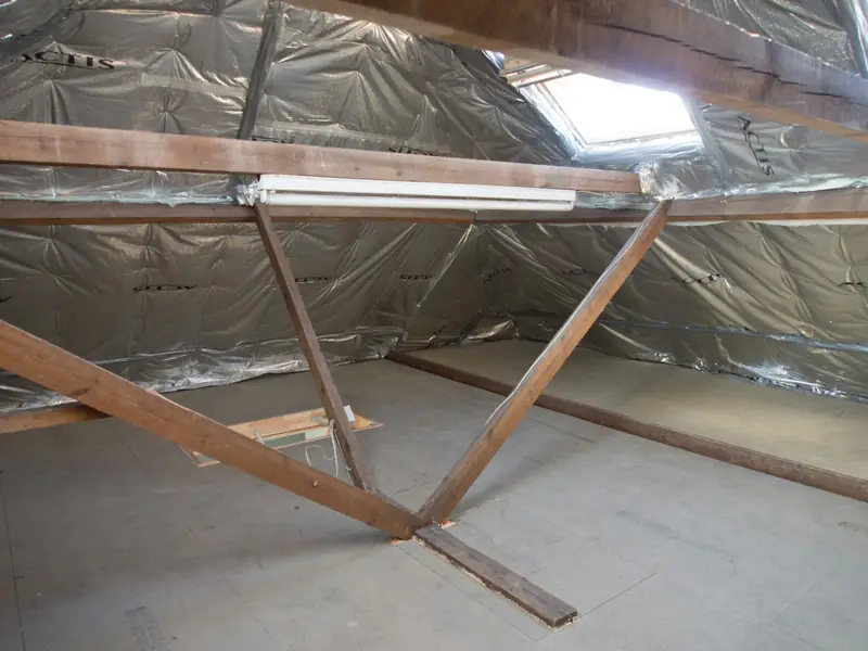 Inside an attic with exposed wood framing, foil-faced insulation and a skylight