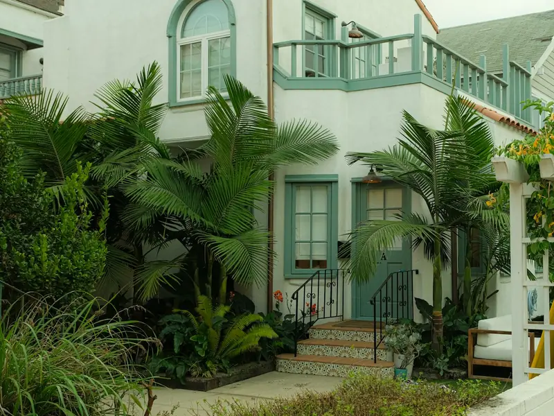 Two-story white stucco home with green trim, palm trees and landscaping